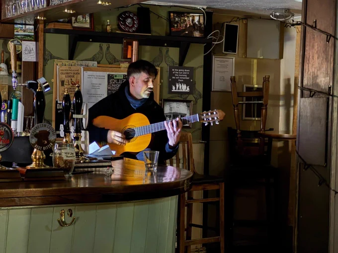 Olie Campbell a man with a guitar sitting at the bar with a spot light on him.