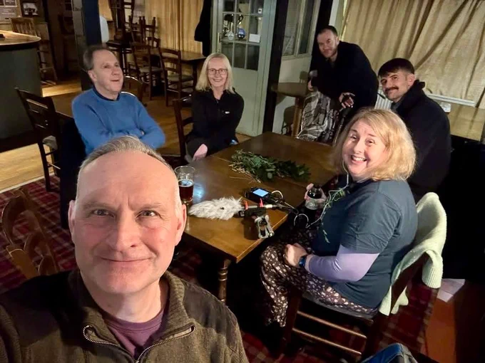 4 men and 3 women sitting around a pub table all smiling at the camera.