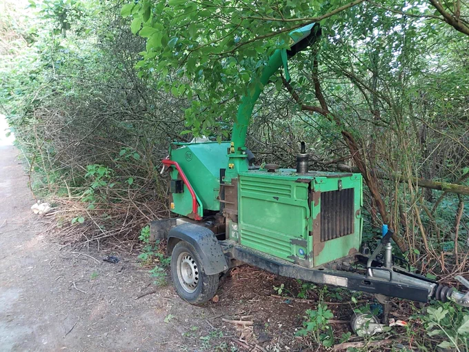Photo of a green wood chipper, concealed in a hedgerow near to a footpath.