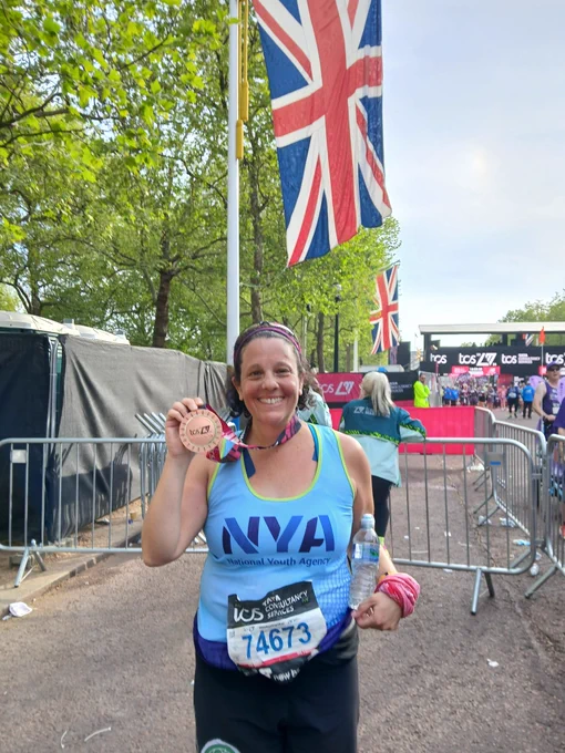 A photo of me at the end of the London Marathon. I'm smiling and holding the medal next to my face 