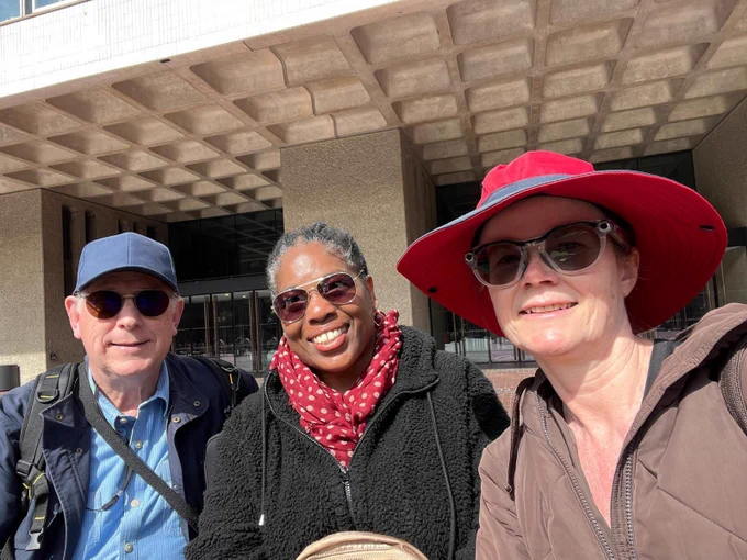 a man with a blue hat, woman with a red scarf and another woman with a red hat smiling with sunglasses.