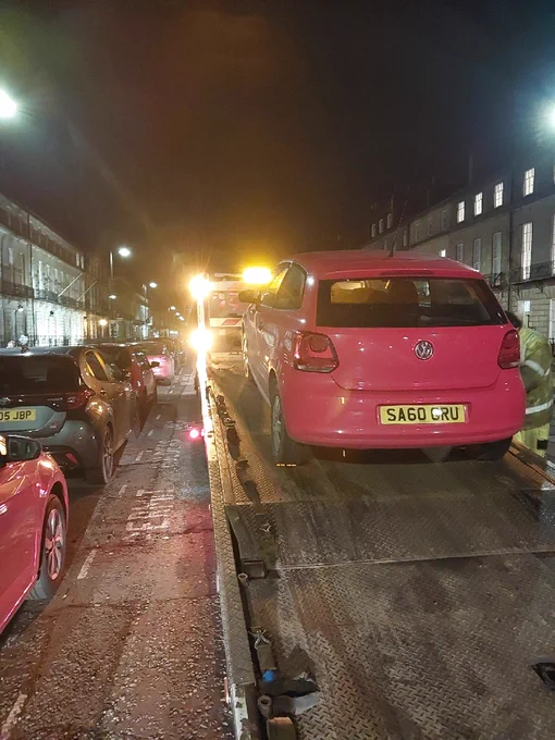 A red Volkswagen Polo being loaded onto a tow truck at night on a street.