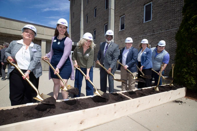 From left to right, UW-Whitewater Interim Provost Robin Fox, State Sen. Melissa Ratcliff, State Rep. Brienne Brown, UW-Whitewater Chancellor Corey King, State Sen. Mark Spreitzer, Rep. Joan Fitzgerald, and a UW-Whitewater representative wear hard hats and hold golden shovels with dirt in the groundbreaking ceremony.