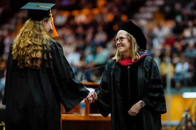Michigan Tech graduate in cap and gown shaking hands with faculty member during a university commencement ceremony.