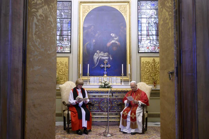 Pope Leo XIV and Archbishop Sarah are seated side by side in the service after their audience, wearing ornate robes, in a chapel. Behind them is a large painting depicting a biblical scene, flanked by stained glass windows. A cross is between them on a small table with candles. The setting exudes a solemn and sacred atmosphere.
