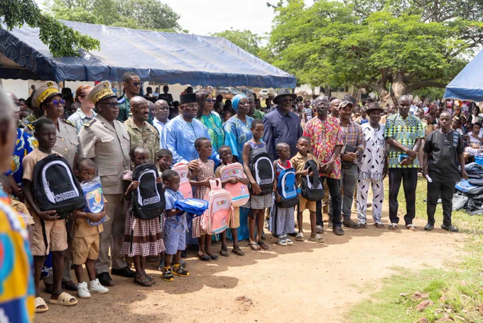 A U.S. Army Soldier in camouflage uniform and beret stands in the center of a group of local children and village elders in Ouffoué-Diékro. Everyone is gathered together in a friendly pose in front of a primary school building, showcasing a moment of community engagement during Exercise Flintlock 26.