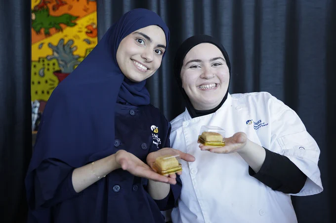 Two smiling people are holding desserts in their hand.
