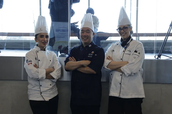 Three people wearing chefs uniforms stand together with their arms crossed. 
