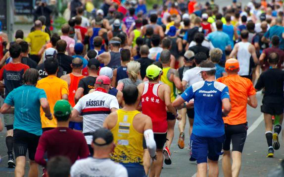 Large group of runners participating in a marathon on a city street, wearing colorful athletic gear and caps.