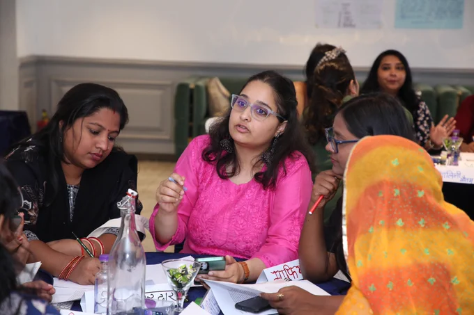 Close-up of participants at CREA’s FLMBaRI Hindi Institute in discussion, with one woman in a pink top speaking and gesturing while others listen and refer to their notes.
