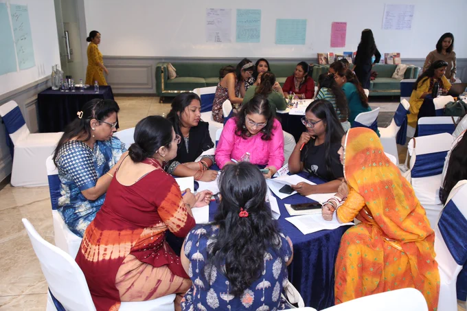 Participants at CREA’s FLMBaRI Hindi Institute work collaboratively around a round table, writing and discussing ideas during a group activity, with posters on the wall behind them.
