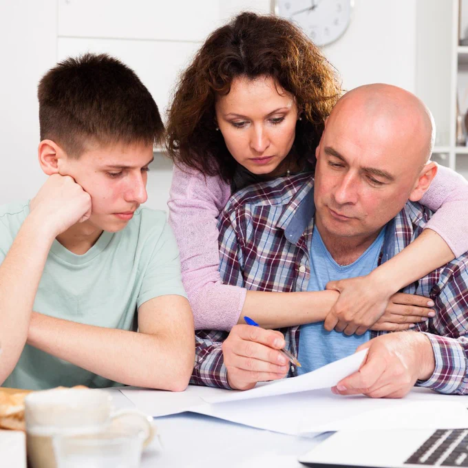 A mother, father, and teenage son sit together at a kitchen table reviewing paperwork, representing families navigating the Disability Tax Credit application process in BC.
