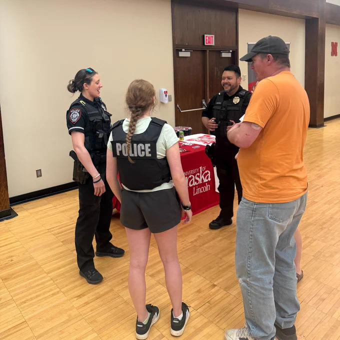 Two police officers speak with a student wearing a police vest and another attendee at a University of Nebraska–Lincoln table during a criminal justice career fair.