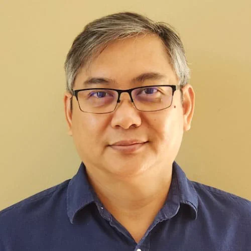 Person wearing a navy blue collared shirt against a plain beige background.