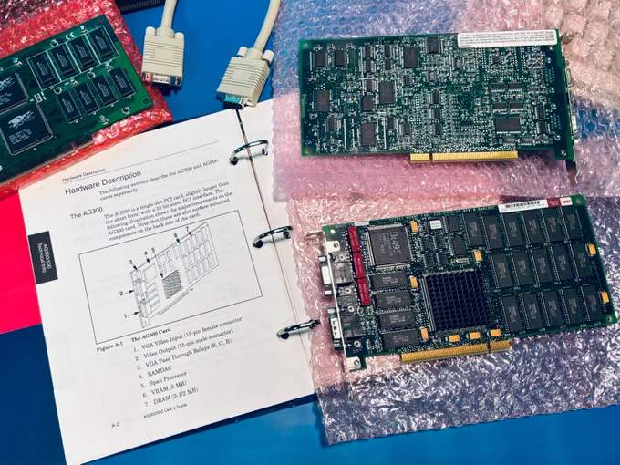 On the left: opened spiral notebook guide for the AG300 and a 3dfx voodoo. Two AccelGraphics AG300 boards on the right.