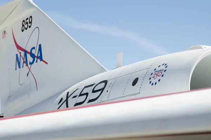 Close up view of NASA’s X 59 aircraft tail and rear fuselage showing the NASA logo, X 59 text, and a small Freedom 250 emblem near the engine area against a blue sky.