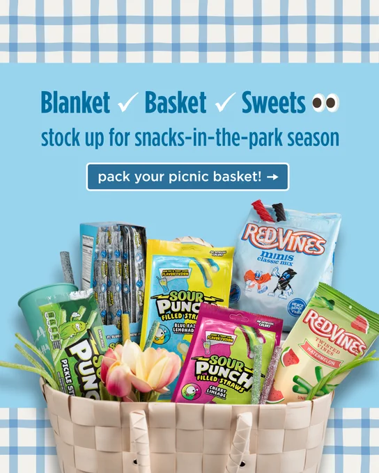 A picnic basket filled with various snacks including Red Vines, Sour Punch candies, and a colorful array of tulip flowers. The background features a blue and white checkered pattern and text encouraging stocking up for snacks-in-the-park season.