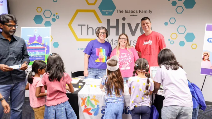Three adults smiling and standing behind a table with children conducting an activity.