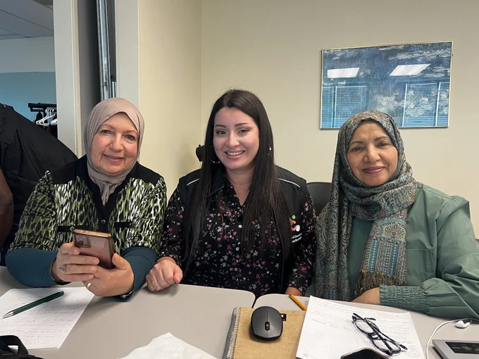 Three women seated at a table during a Connected Canadians session, with notebooks, a phone, and learning materials in front of them.