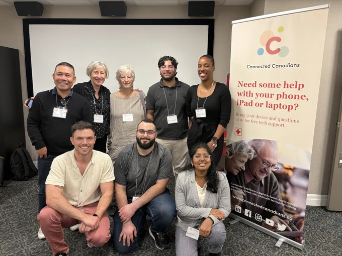 A group of Connected Canadians volunteers smiling together in front of a Connected Canadians banner.