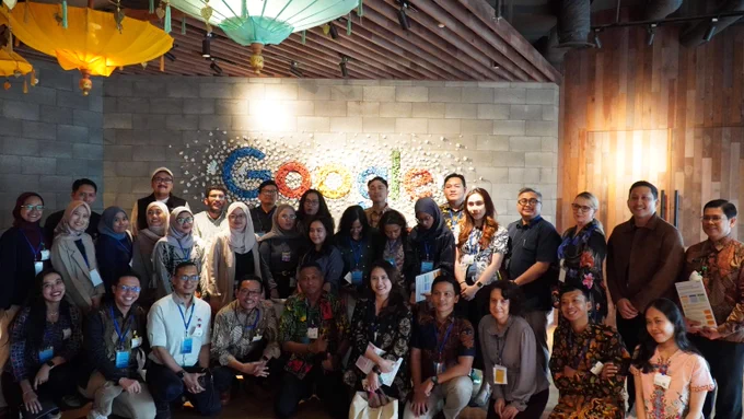 Group photo of participants employees posing in front of a colorful Google logo on a brick wall inside a modern office space.