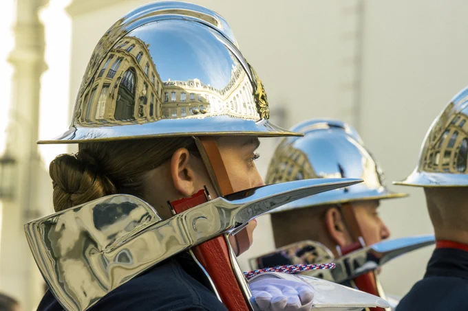 Photographie de trois pompiers avec des casques reflétant la cour de l'Hôtel de Beauvau. Ils tiennent une hache. 