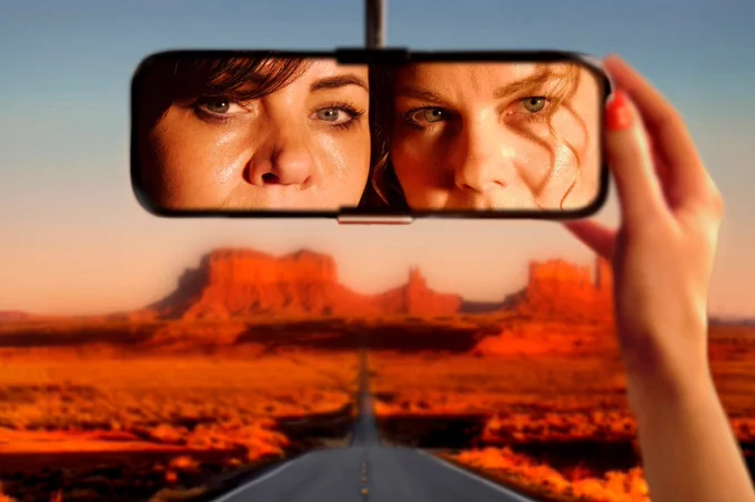 A photo showing two women looking into a back mirror in a car 