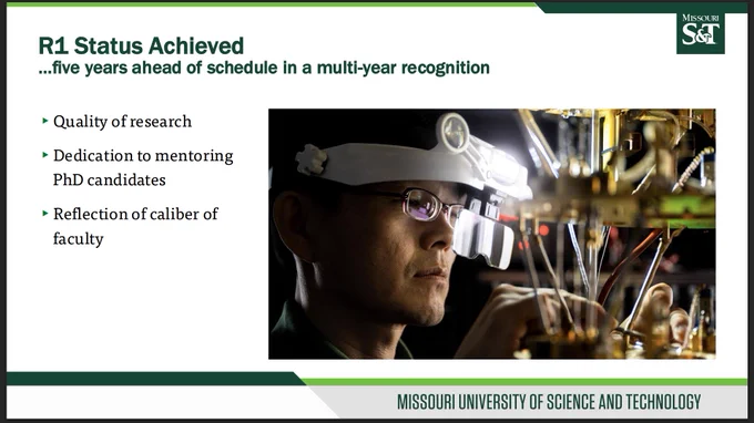 Slide titled “R1 Status Achieved,” with a subtitle noting five years ahead of schedule in a multi-year recognition. On the left, three bullet points read: Quality of research; Dedication to mentoring PhD candidates; and Reflection of caliber of faculty. On the right, a large photo shows a researcher wearing magnifying headgear working with laboratory equipment in a controlled research environment. Missouri S&T branding appears on the slide.