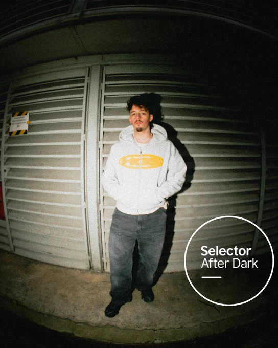 Daviaa stands casually with hands in his pockets against a metal shutter, lit by a harsh flash, while a circular “Selector After Dark” logo with white text and a thin border appears in the corner.
