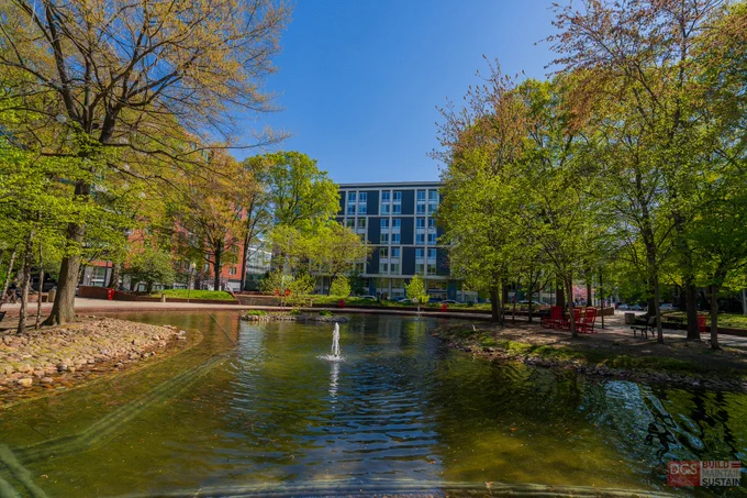 Calm SW Duck Pond with a small fountain surrounded by green trees and a modern building in the background under a clear blue sky