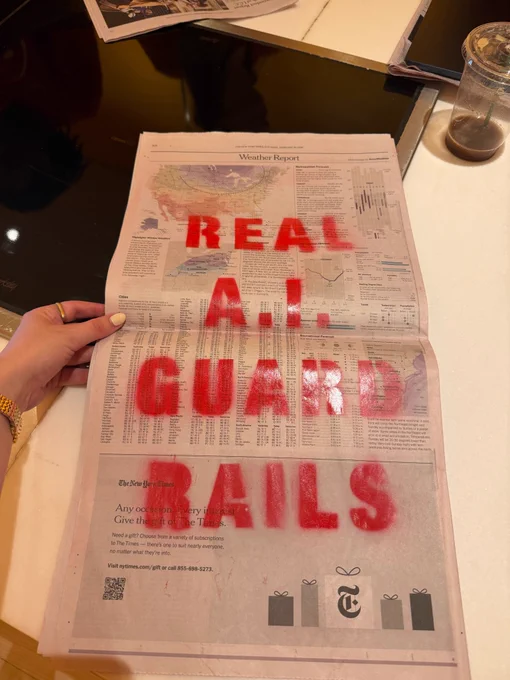 A copy of The New York Times with a spray painted message that says "REAL A.I. GUARD RAILS."