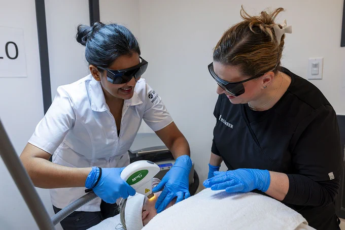 Two people wearing safety goggles are using a device to provide treatment to a client.
