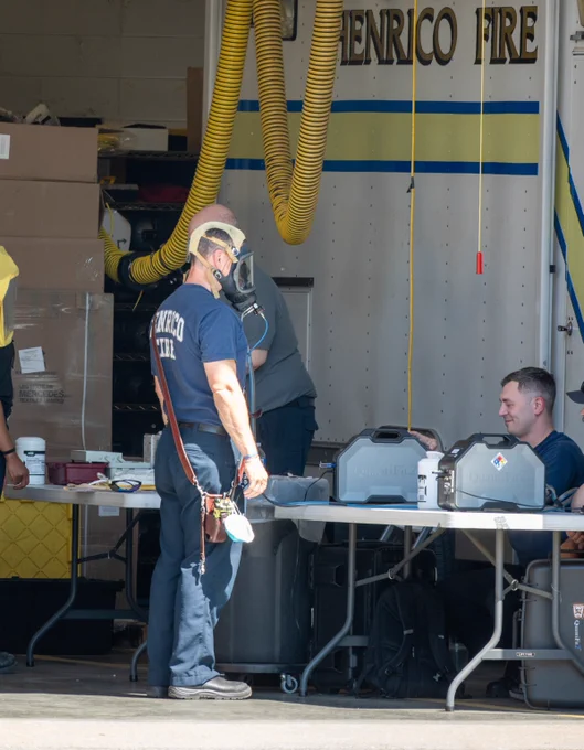 Firefighter wearing a SCBA mask stands near a table with equipment inside a fire station garage.