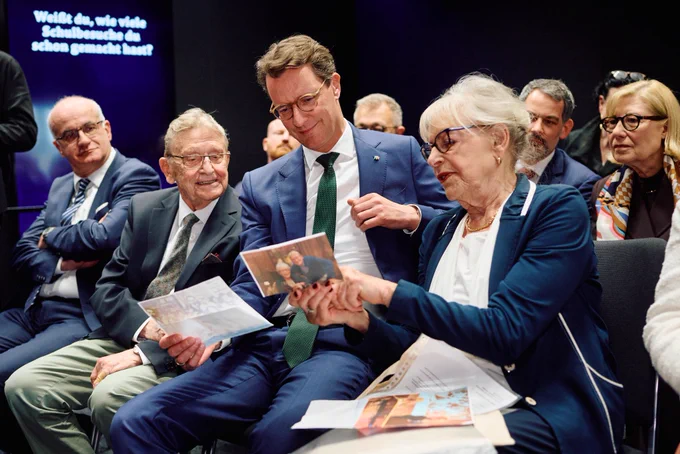 Ministerpräsident Hendrik Wüst schaut sich mit einem älteren Mann und einer älteren Frau ein Bild an.