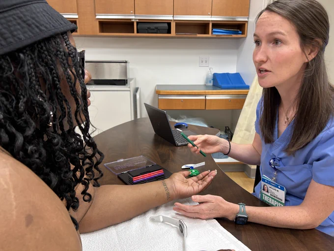 A hand occupational therapist is sitting across a patient in a clinical setting.