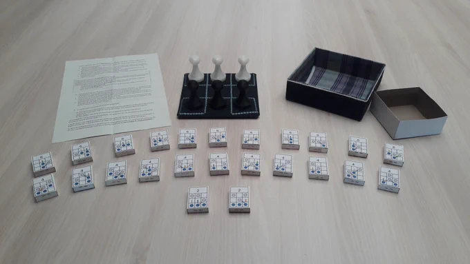 Dispositif de jeu posé sur une table avec un plateau, des pions noirs et blancs et plusieurs cartes à manipuler, pour explorer des logiques ou résoudre des défis de manière ludique.