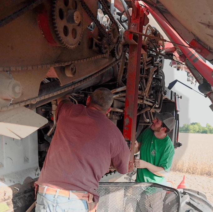 Two men work together to fix a broken part on a combine. 