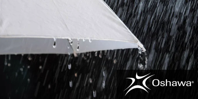 Close-up of a white umbrella with raindrops dripping off its edge during heavy rainfall.