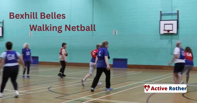 A group of individuals play walking netball in a gymnasium, with a basketball hoop on the wall. Some wear colored bibs with letters. The text reads "Bexhill Belles Walking Netball." A logo for "Active Rother" is in the bottom right corner.