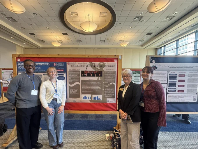 Phia Feigh smiles with peers and Dr. Sara Grove in front of her research poster.