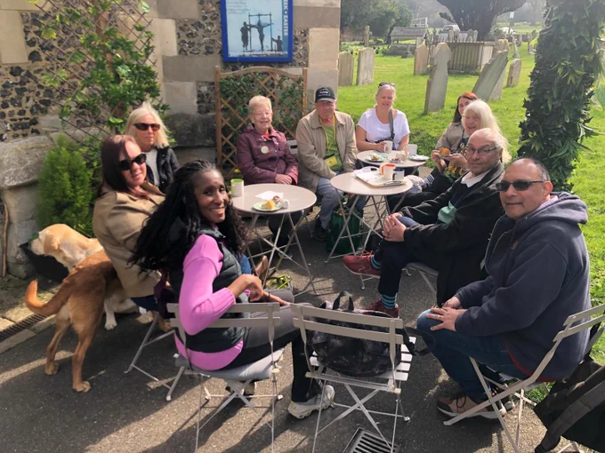 visually impaired group enjoying tea or coffee at an outdoor café table with a two dogs nearby them on a sunny day.