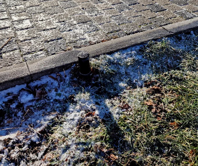 Frozen sprinkler head with frost around it in the grass.