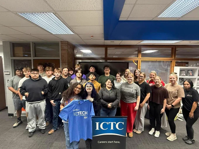 A group of students, some in casual clothing, stand in a room holding a blue sign that says "ICTC".