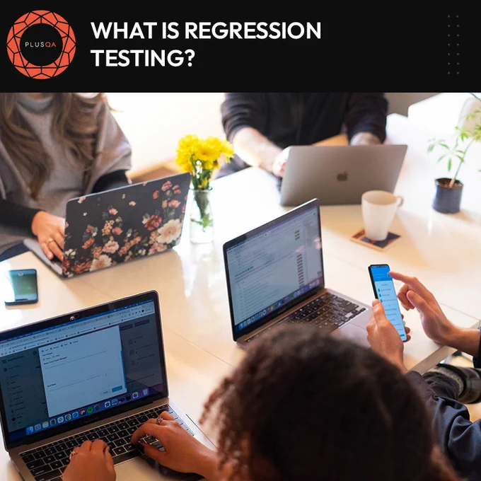 Four QA testers sitting around a table working on laptops and mobile devices.