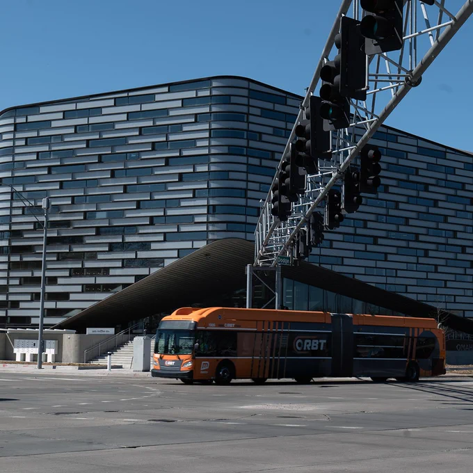 A photo of an ORBT bus driving through the intersection of 72nd & Dodge in front of the Omaha Central Library
