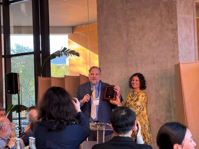 Lampe receiving his award. He is speaking into a microphone while holding a plaque.