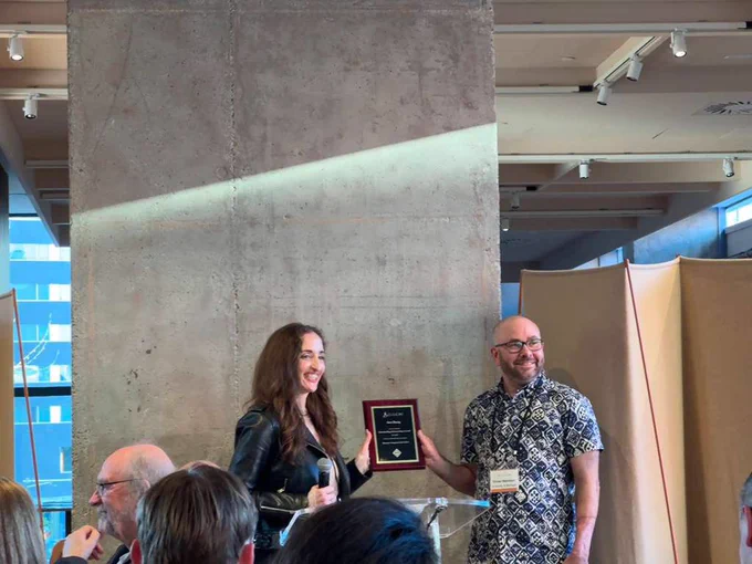 Michaelanne Thomas & Oliver Haimson hold a plaque of Ben Zhang’s award & stand smiling at CHI 2026.