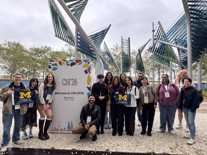 A group of UMSI researchers stand outside at CHI 2026, smiling, in front of a colorful CHI 2026 sign.