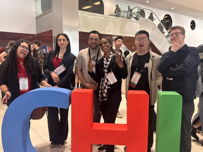 A group of UMSI researchers at CHI 2026 standing inside the convention center, smiling, in front of colorful CHI blocks.