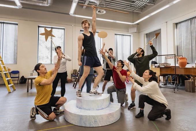 A photo showing a group of performers posing in a rehearsal room with cardboard props 